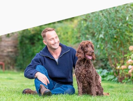 Mand og hans hund sidder på græsset